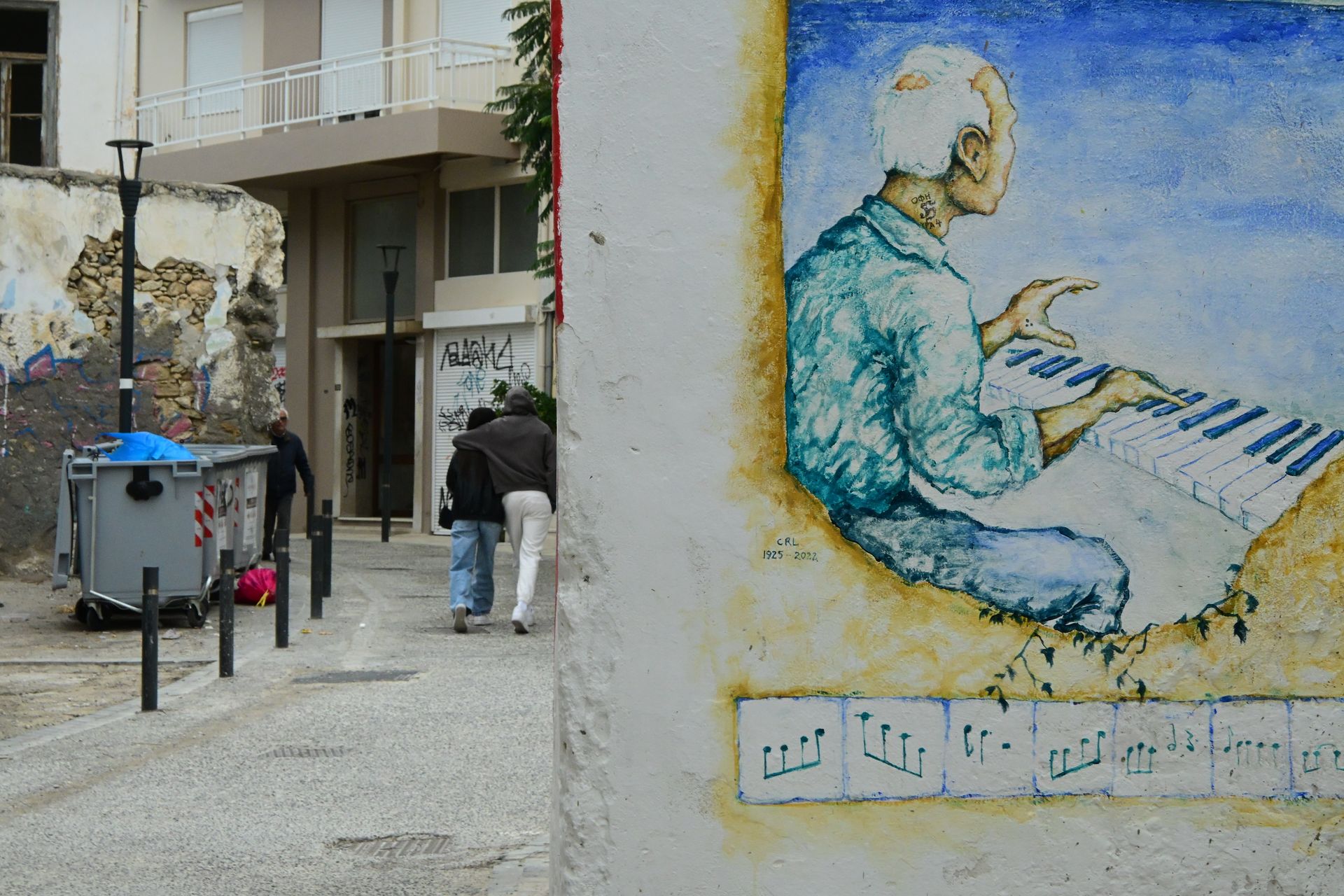 Mural of a seated keyboard player beside a street with apartment buildings and pedestrians