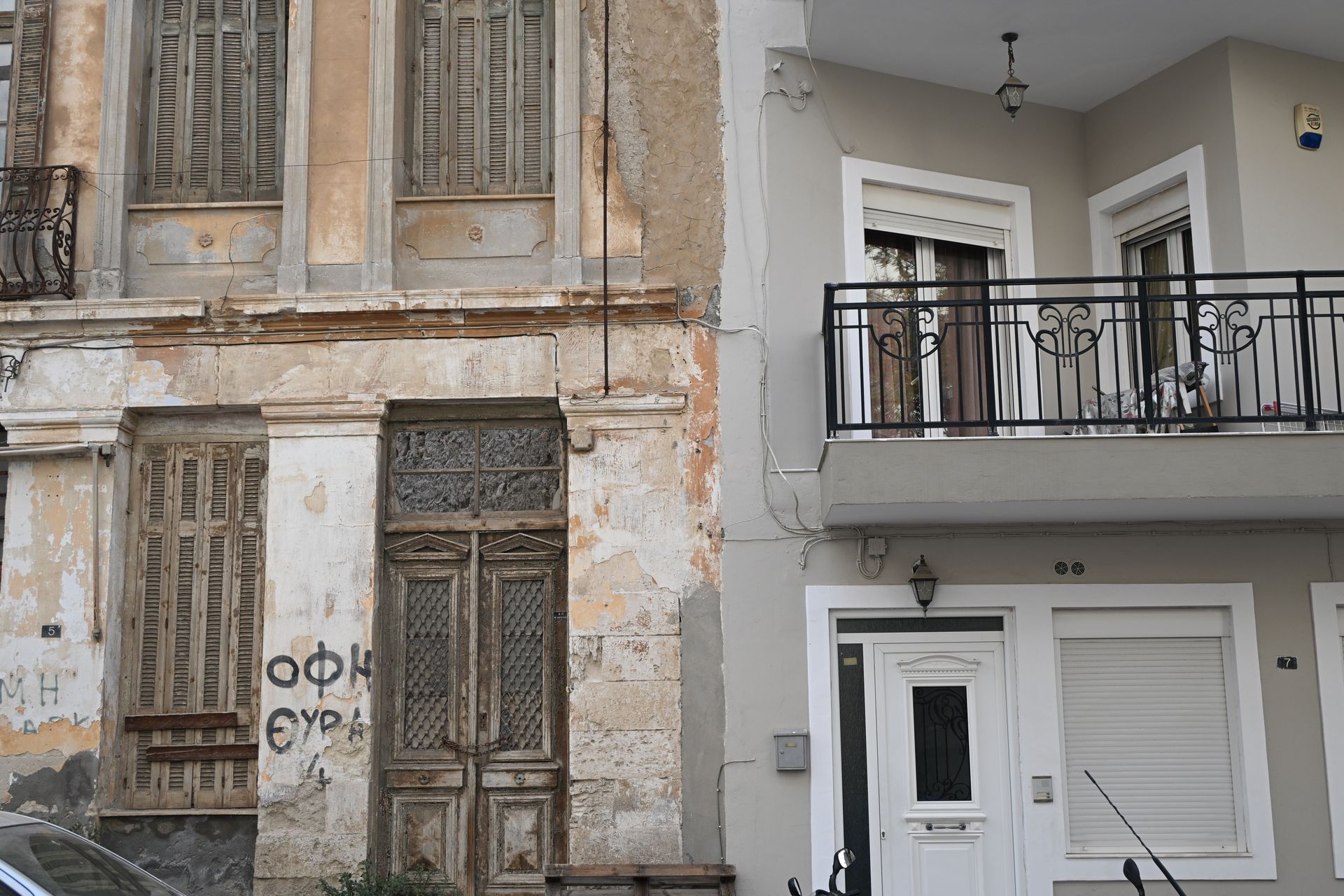Weathered building with boarded windows beside a renovated white facade and balcony